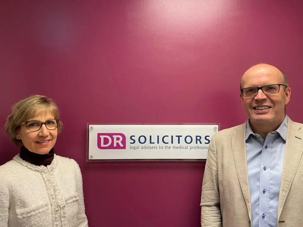 An image of a smiling man and woman in front of the DR Solicitors sign.