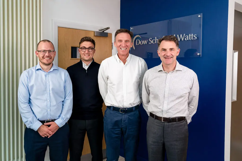 A group of men smiling in front of the Dow Schofield Watts sign.