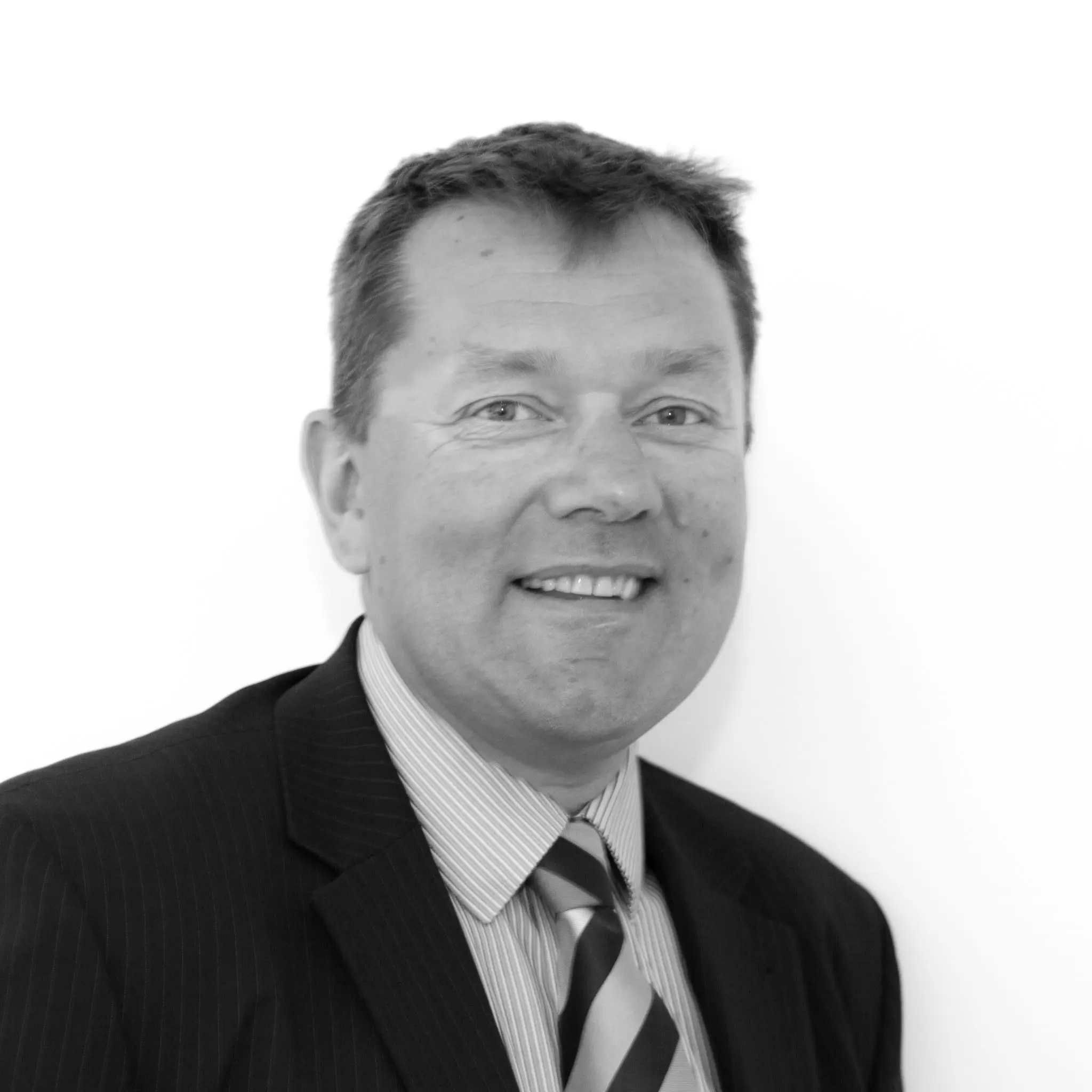 A black and white headshot image of a smiling man against a white backdrop