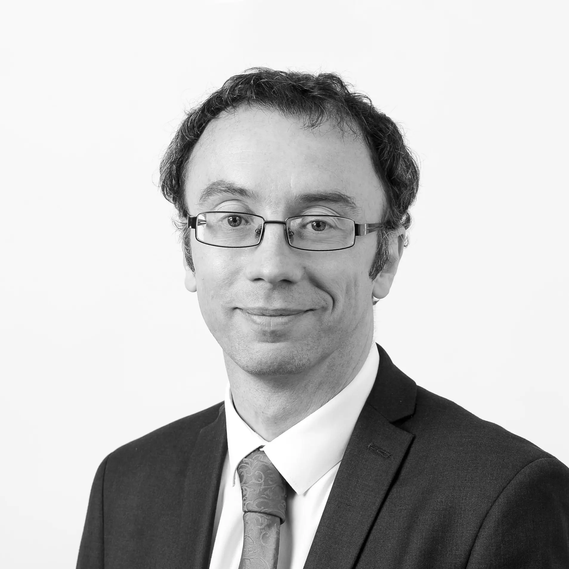 A black and white headshot image of a smiling man against a white backdrop