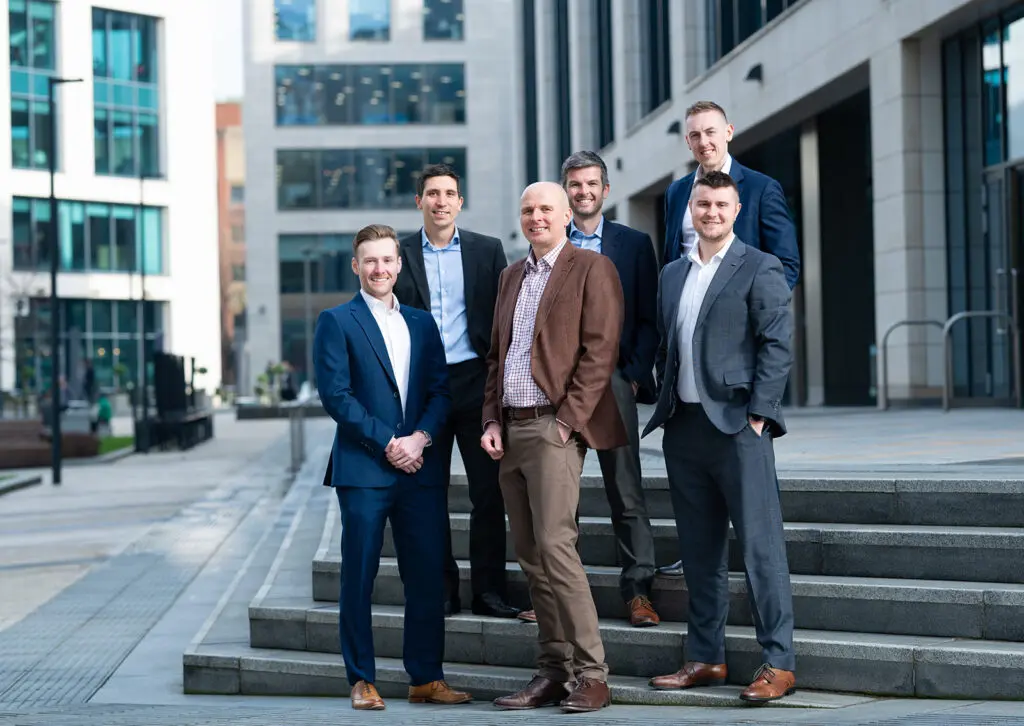 A group shot of smiling men in formalwear stood on steps in front of an office building.
