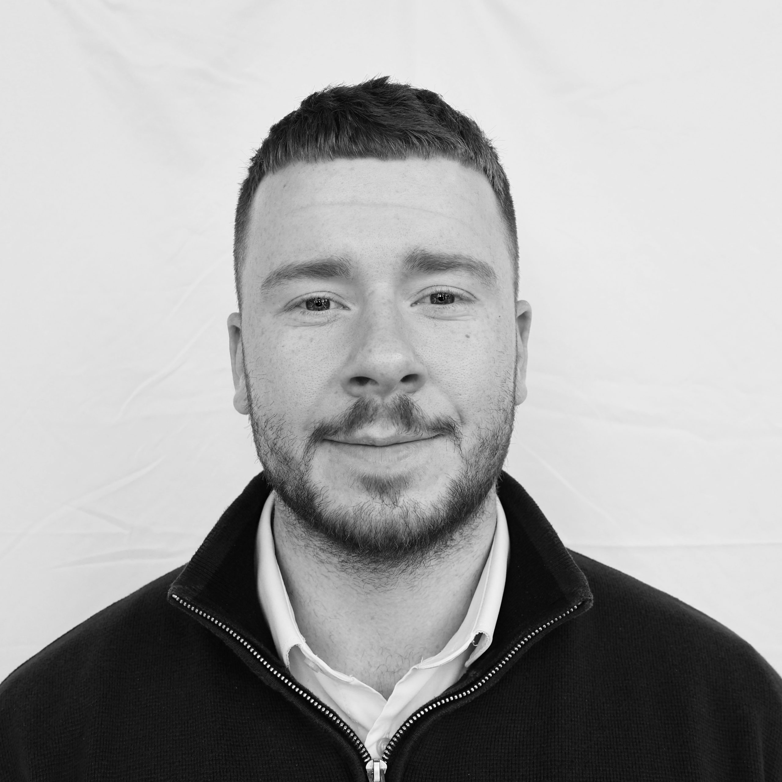 A black and white headshot image of a smiling man against a white backdrop