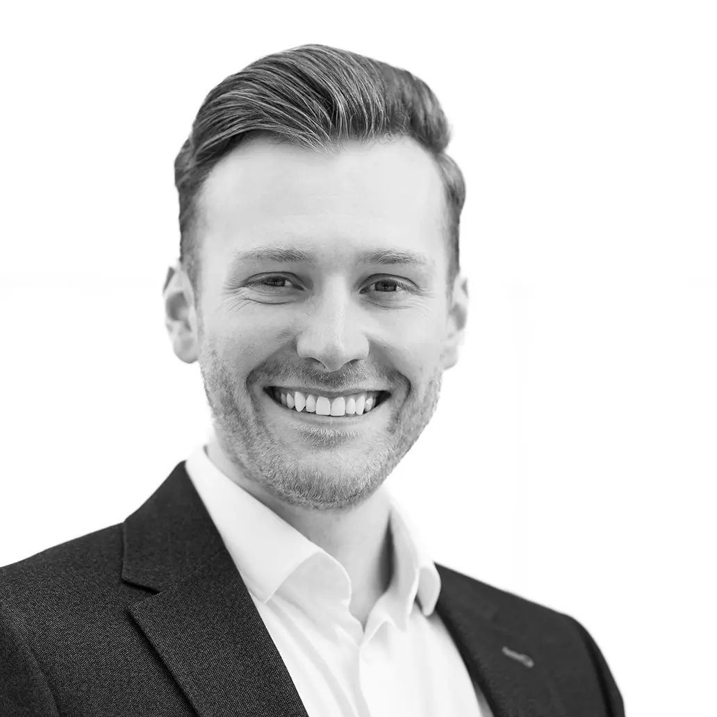 A black and white headshot image of a smiling man against a white backdrop
