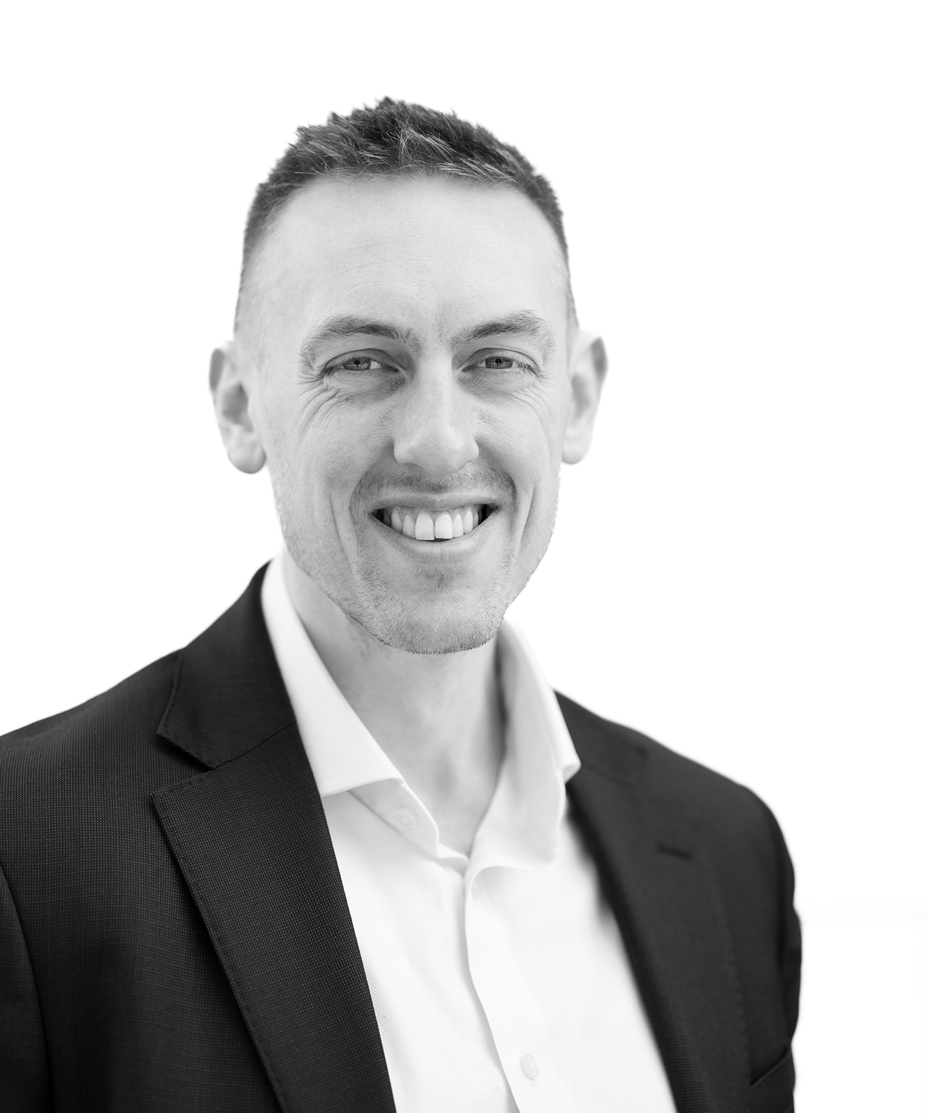 A black and white headshot image of a smiling man against a white backdrop