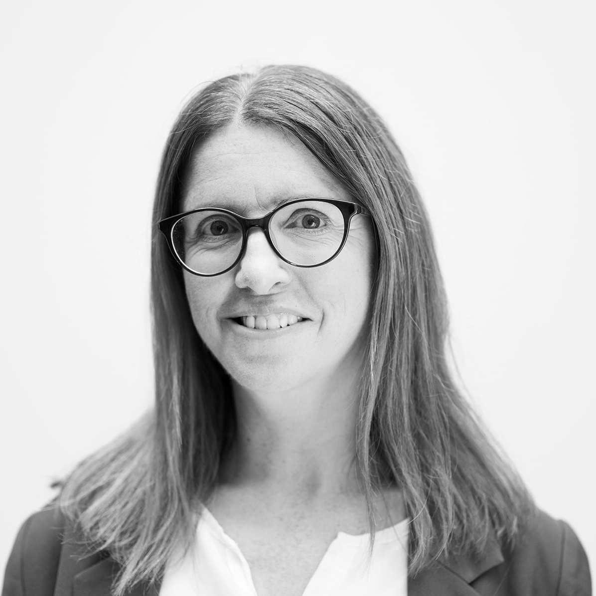A black and white headshot image of a smiling woman with glasses