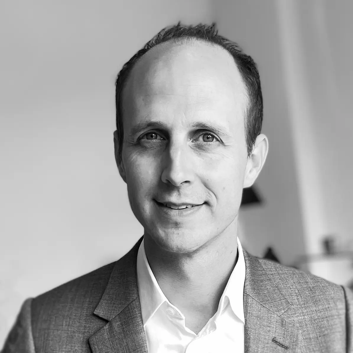 A black and white headshot image of a smiling man against a white backdrop