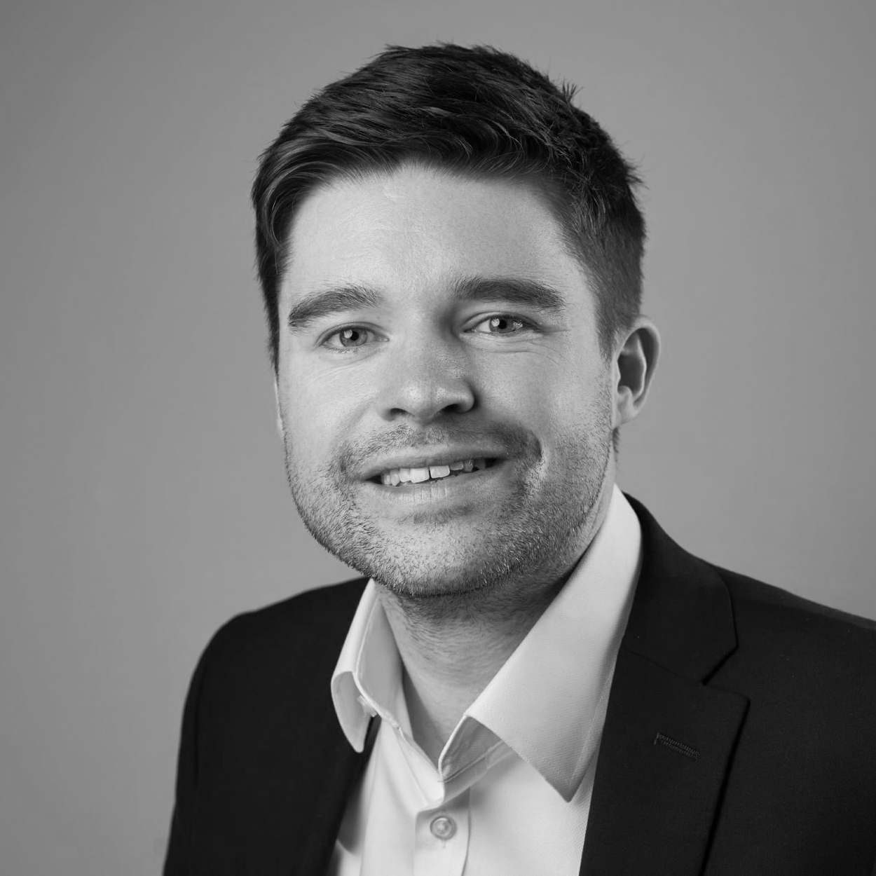 A black and white headshot image of a smiling man against a white backdrop