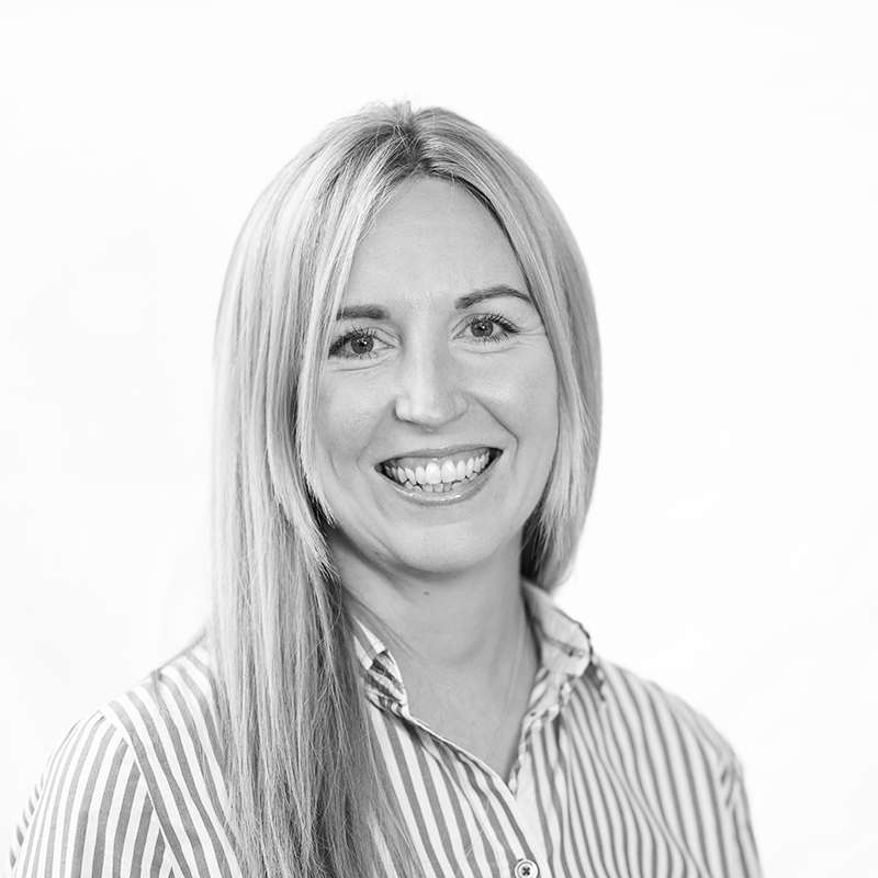 A black and white headshot image of a smiling woman against a white backdrop