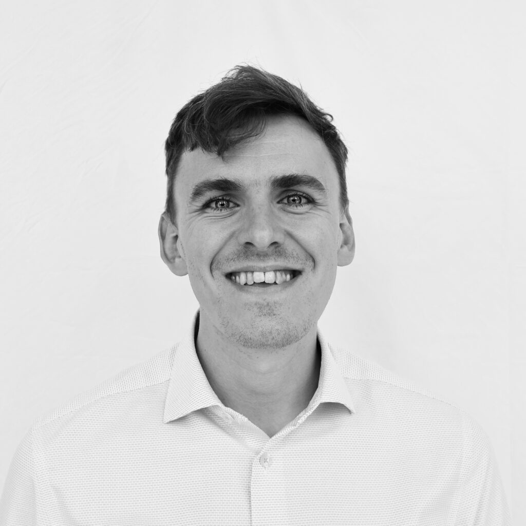 A black and white headshot image of a smiling man against a white backdrop