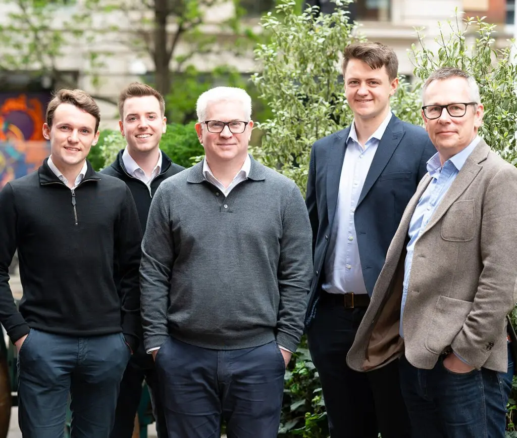 A team of male employees standing and smiling together in a garden setting.