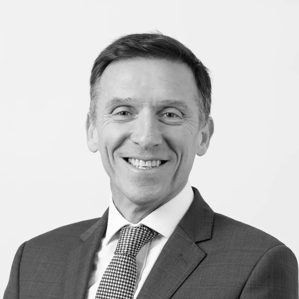 A black and white headshot image of a smiling man against a white backdrop
