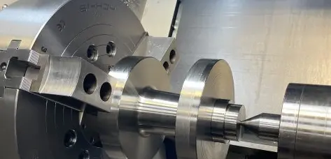 A close-up of a CNC machine or lathe, actively shaping a metal component, with the finished piece visible in the foreground.