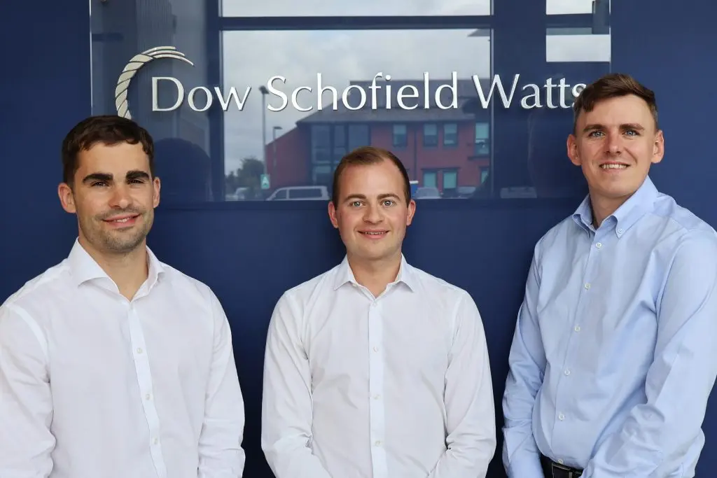 Three smiling men in front of the Dow Schofield Watts logo for their promotion.