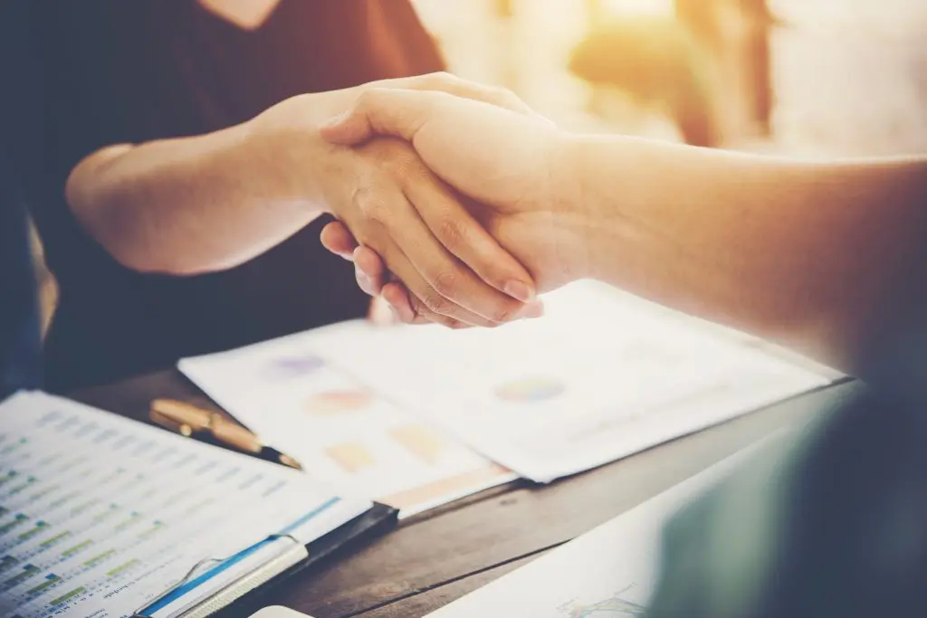 A close up of two business people shaking hands while sitting in a professional setting.