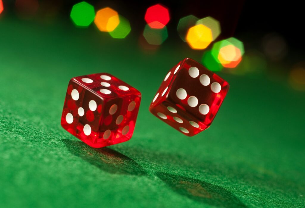 Two red dice with white spots are rolling on a green surface.