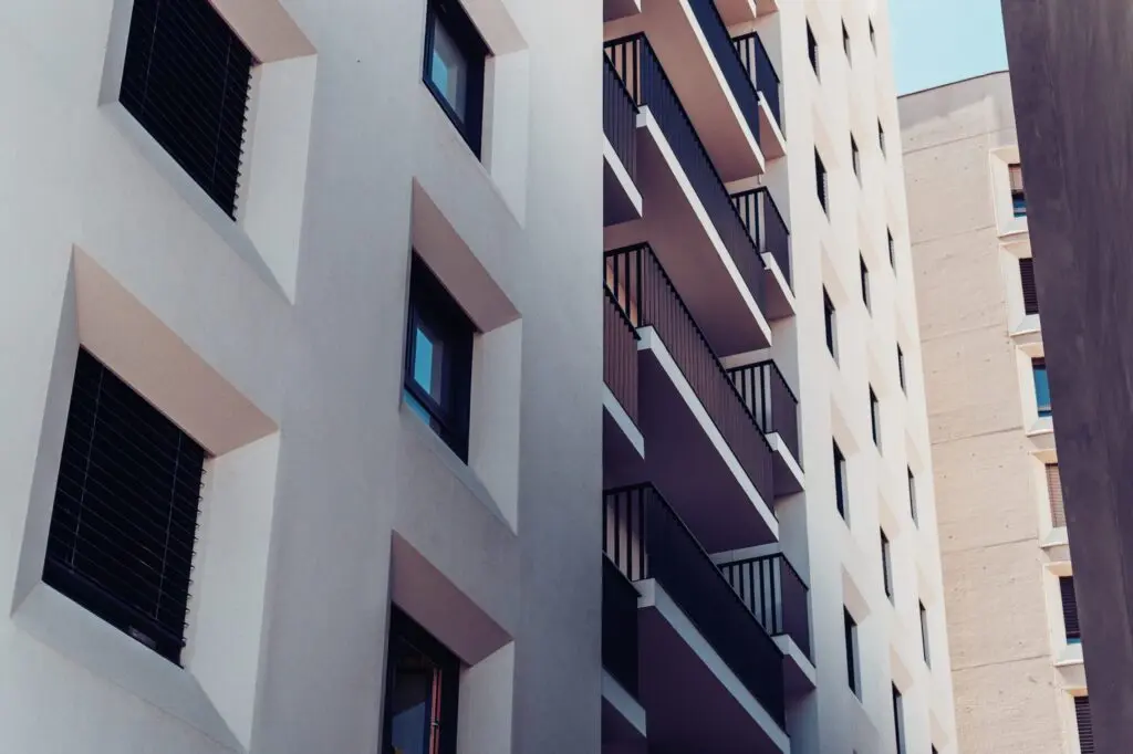 A modern apartment building with white facades, small balconies, and window blinds.