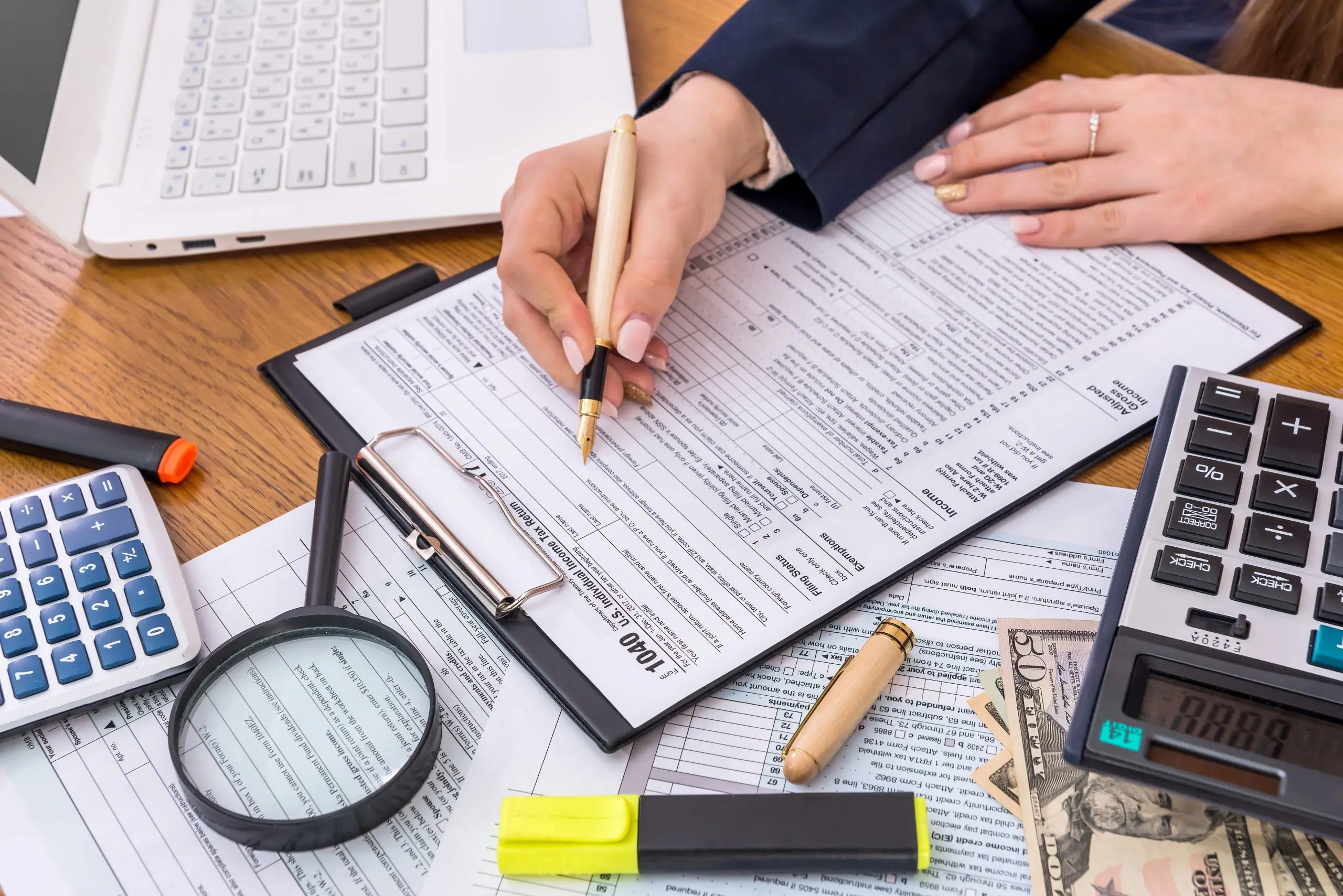 A pair of hands filling out a tax document surrounded by different office stationery.