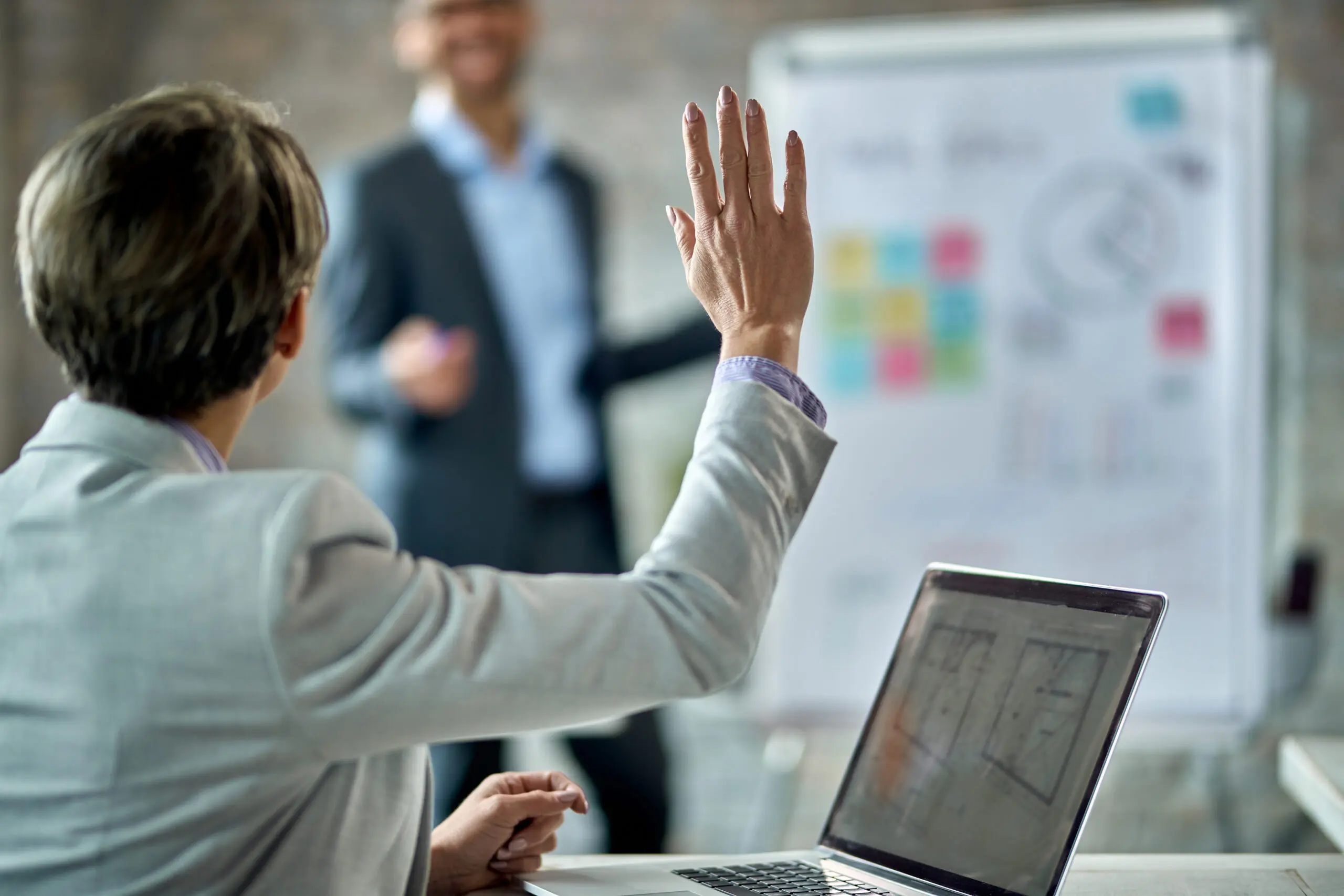 Back view of female entrepreneur raising hand to answer the question during business presentation in the office.