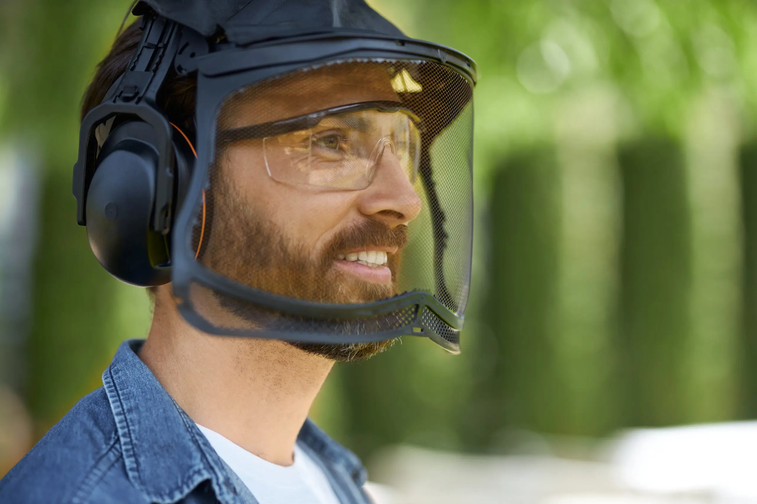 Close-up view of a bearded craftsman in a protective face shield preparing for hard work outdoors.