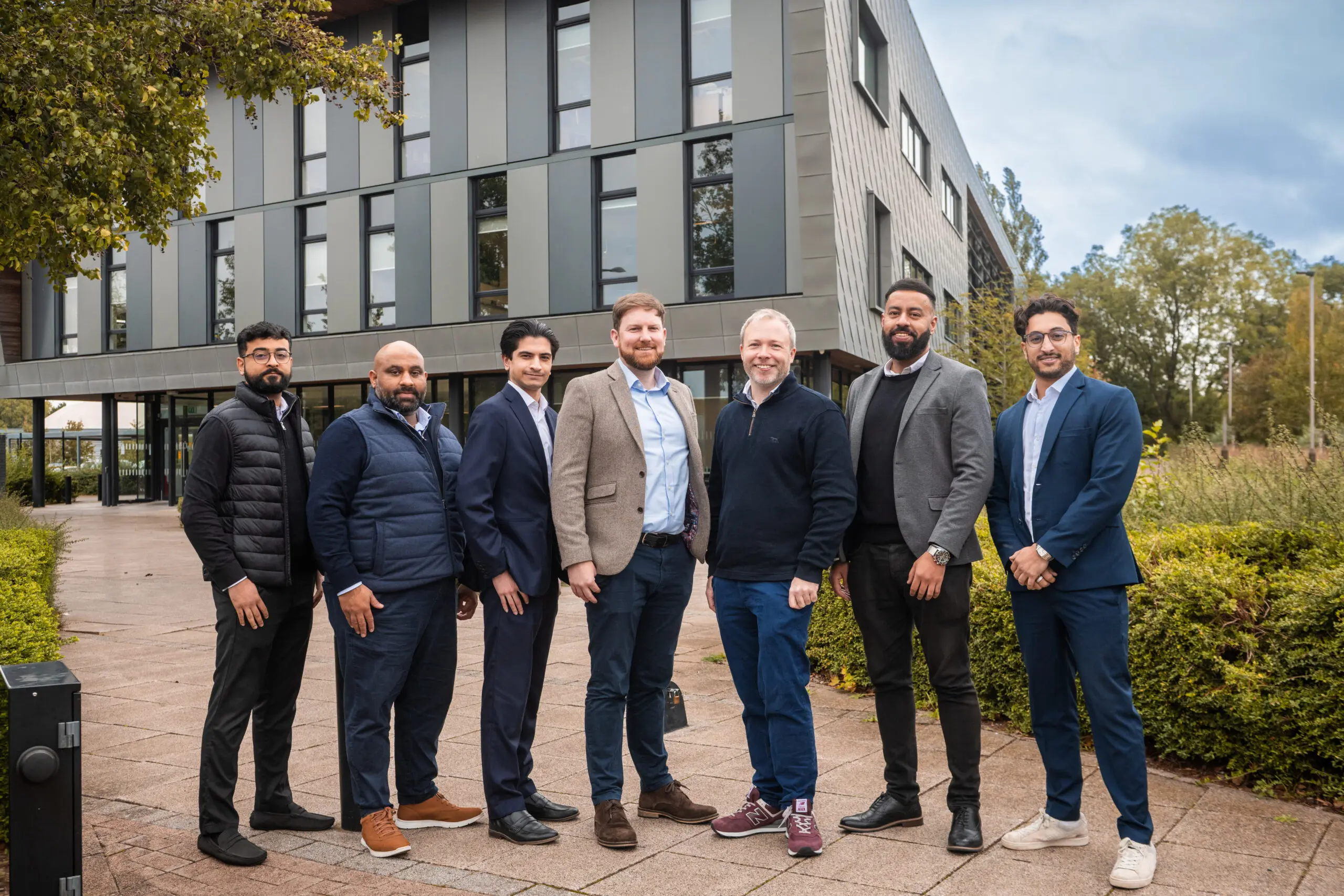 A group of smiling men in casual and businesswear in front of an office building